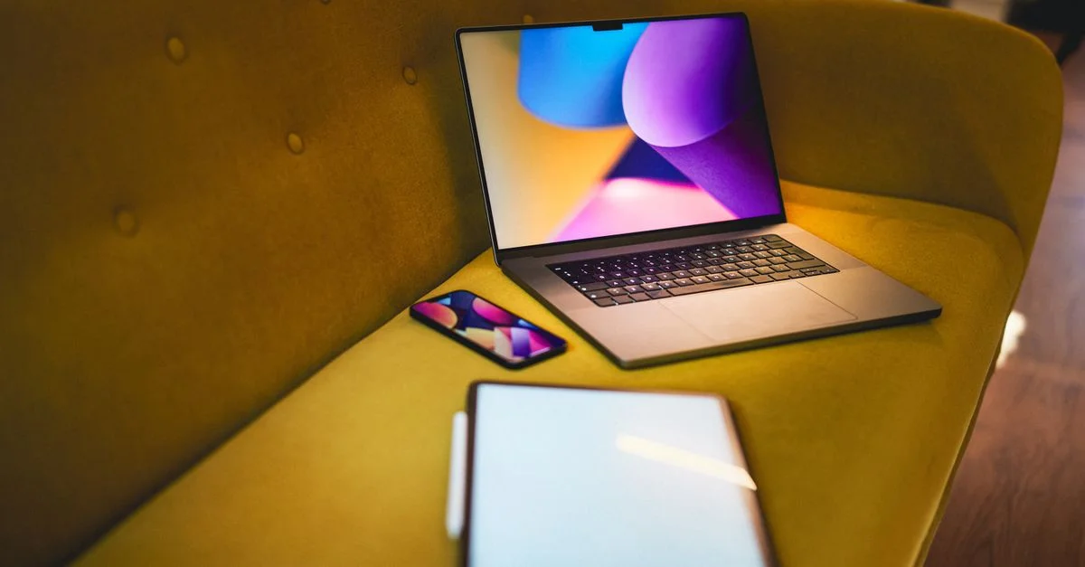 Un cadre de bureau à domicile confortable avec un ordinateur portable, un smartphone et une tablette sur un canapé jaune.